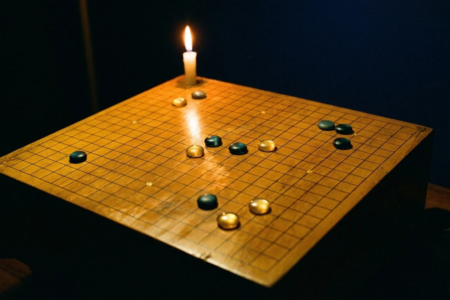 A wooden Go board lit by candlelight, golden Sun and teal Moon stones surrounding empty crossings, star points glowing, The Field of Stars